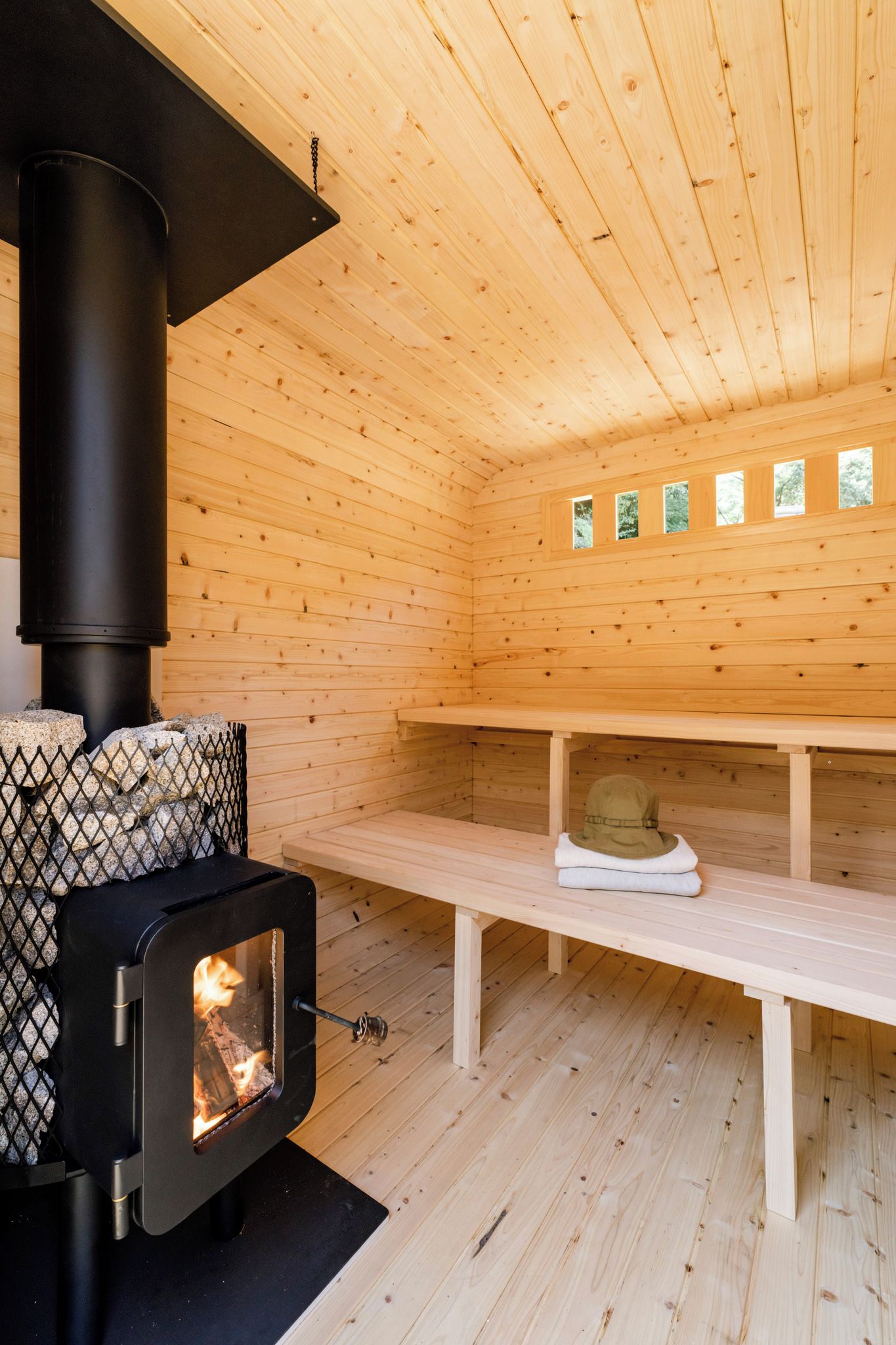 A wooden cabin interior with a wood-burning stove, benches, and a stone fireplace.