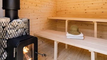 A wooden cabin interior with a wood-burning stove, benches, and a stone fireplace.