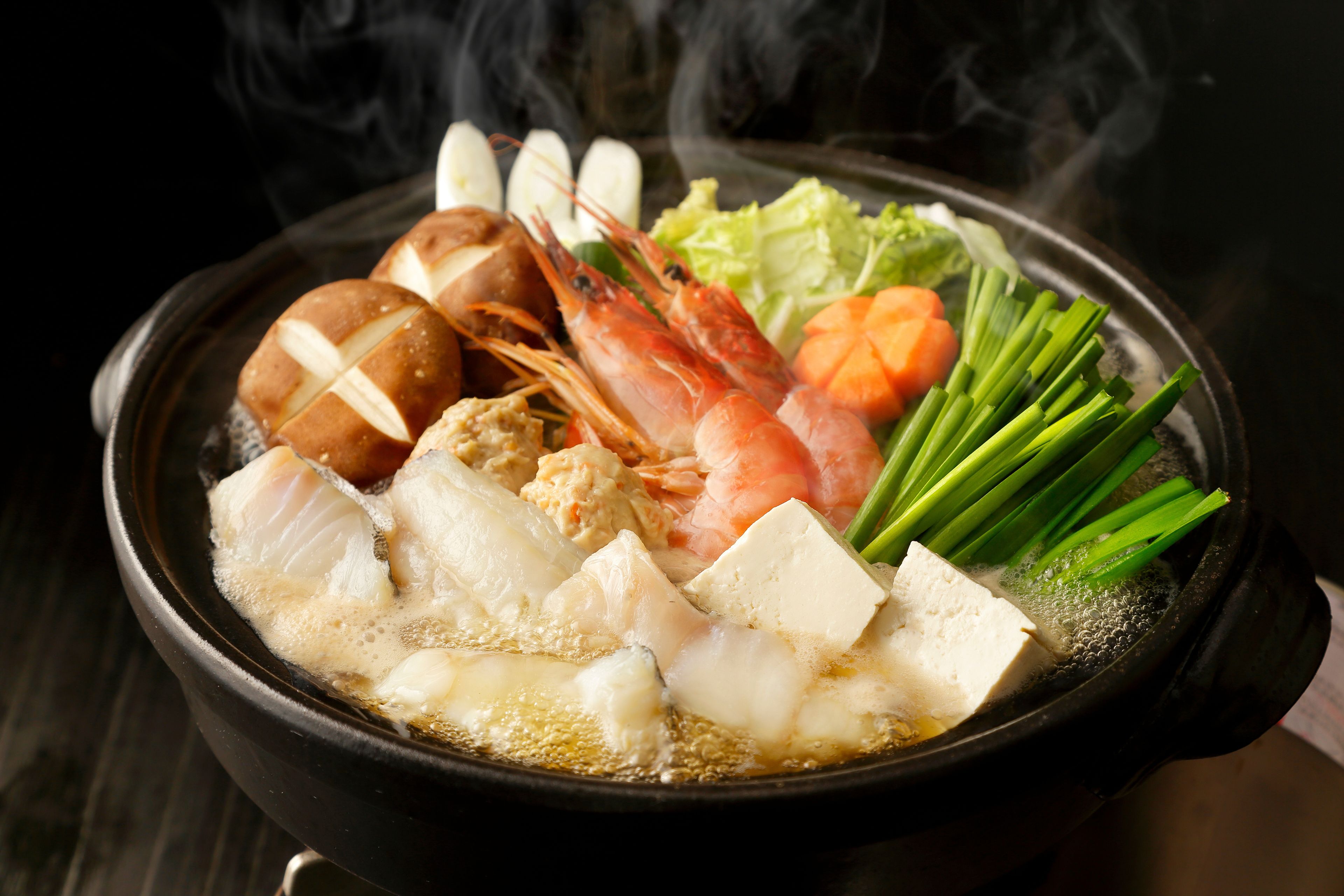 A bowl of hot pot with various ingredients like shrimp, tofu, and vegetables.