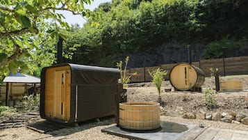 A rustic outdoor setting with wooden structures, including a covered seating area and a hot tub.
