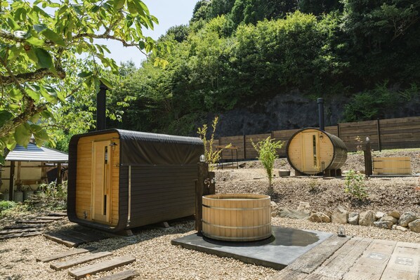 A rustic outdoor setting with wooden structures, including a covered seating area and a hot tub. - Tsuzuya Village, a guesthouse with a full-fledged private sauna (Minokamo)