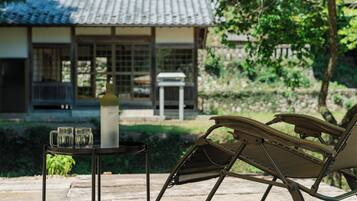 A traditional Japanese-style building with a tiled roof, a garden with a stone pathway, and a lounge chair with a metal frame.