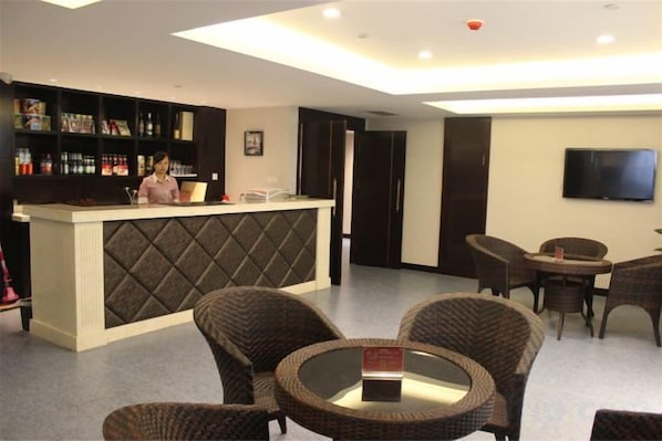 Un hall de hotel con mostrador de recepción, zona de estar y un televisor montado en la pared.