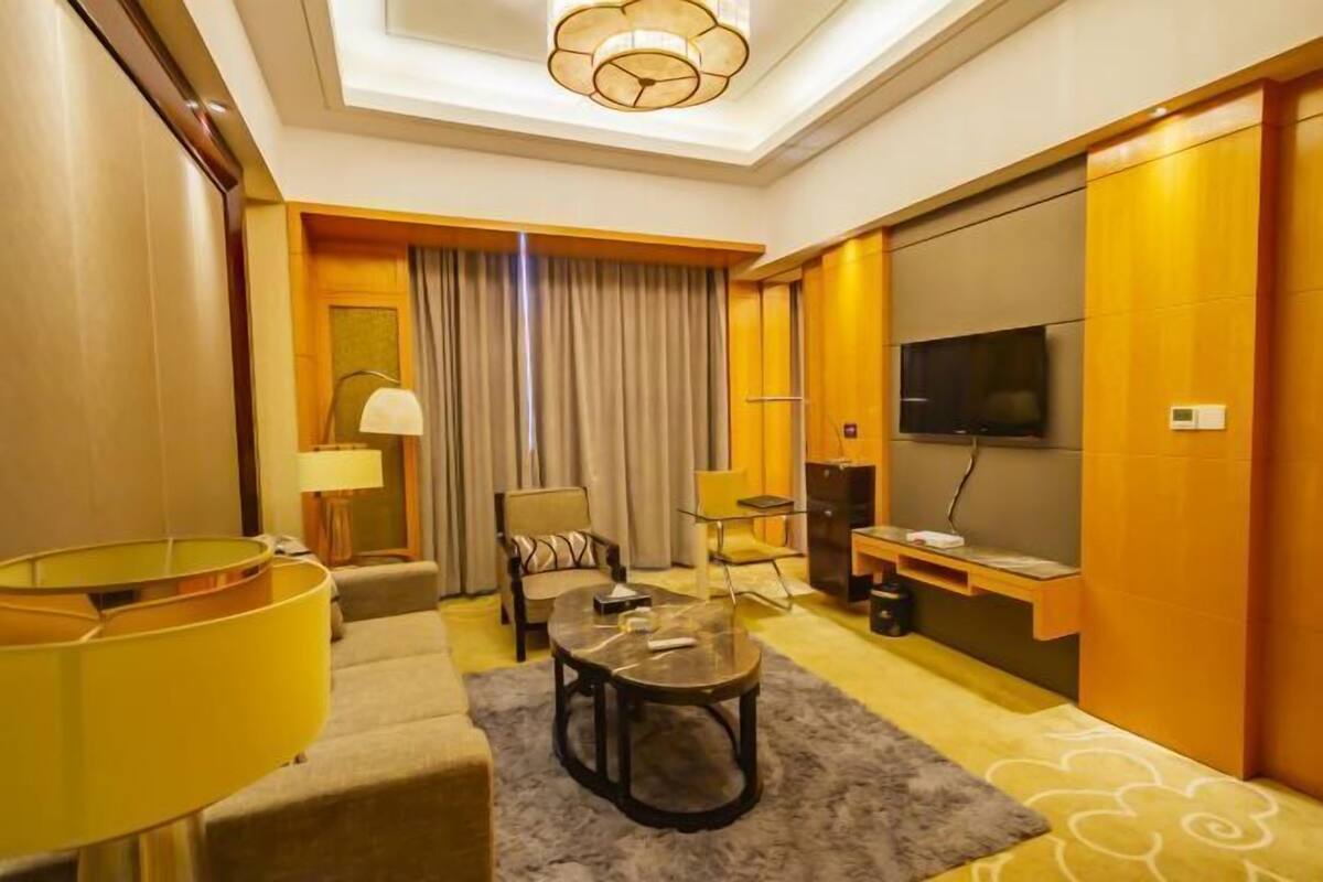 Een hotelkamer met een bank, fauteuil, salontafel, televisie en een bureau met lamp.