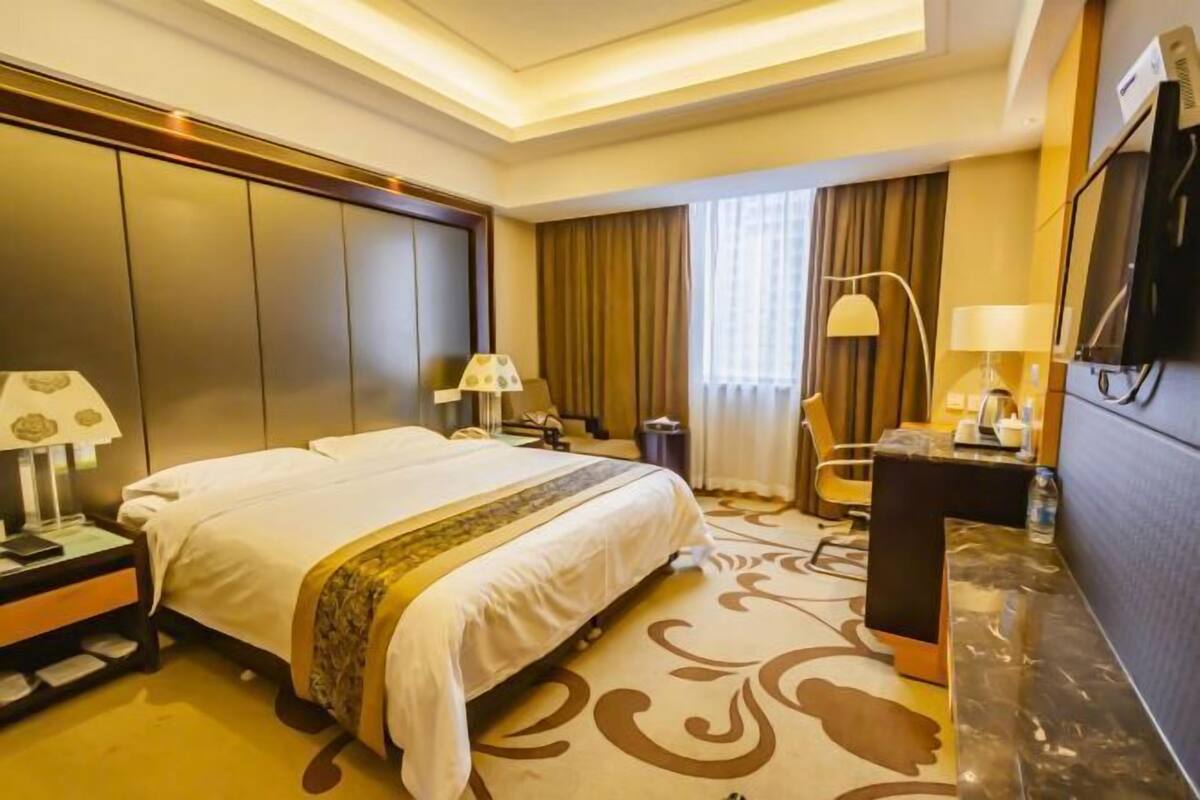 Een hotelkamer met een groot bed, een bureau, een stoel, een televisie en een raam met gordijnen.