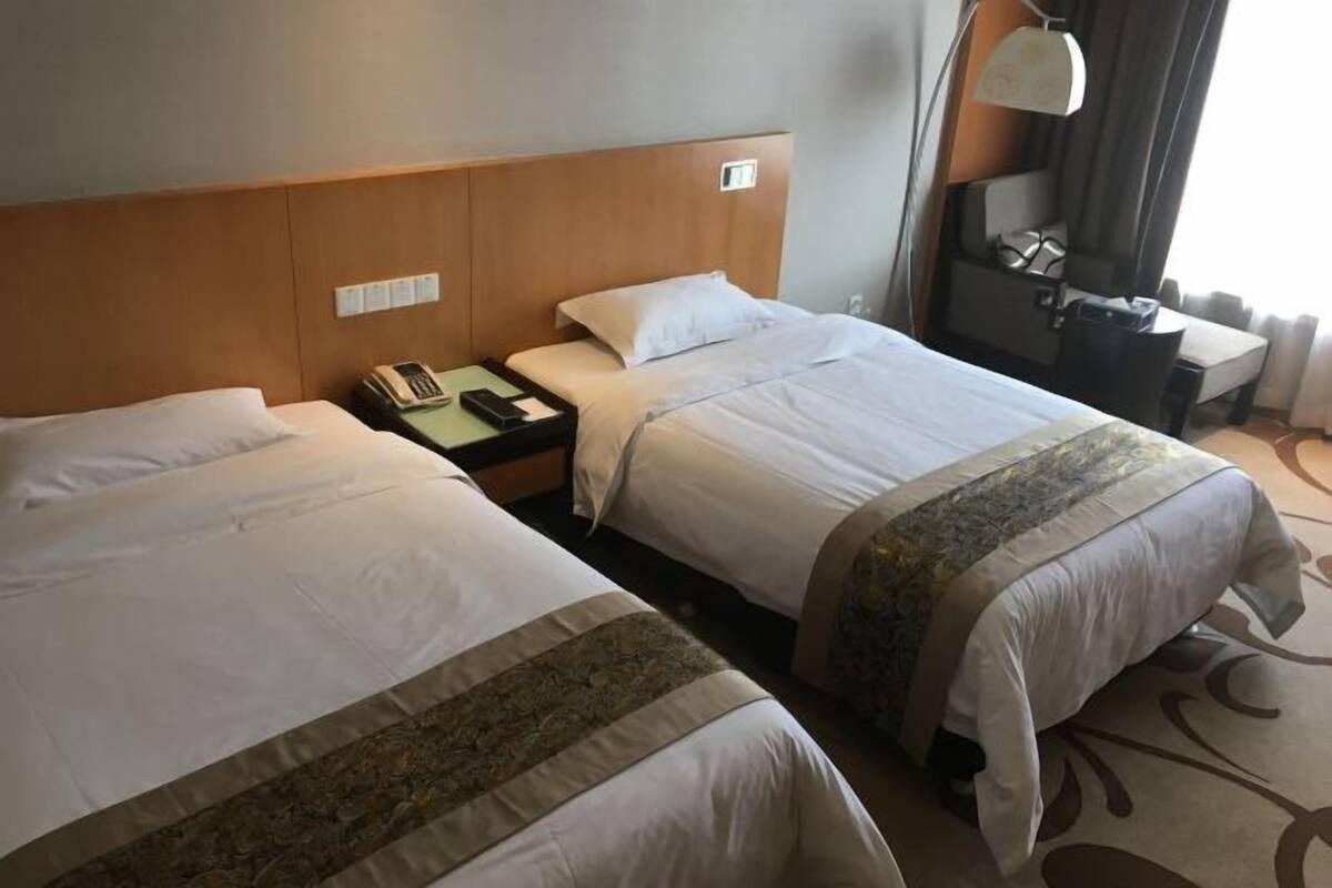 Een hotelkamer met twee bedden, een nachtkastje met een lamp, een telefoon en een klein bureau met een stoel.