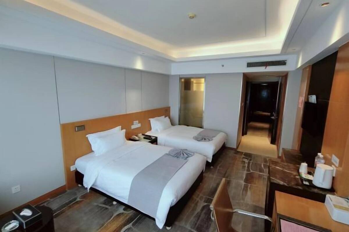 Hotelkamer met twee bedden, een bureau, een stoel, een nachtkastje en een deur naar de badkamer.