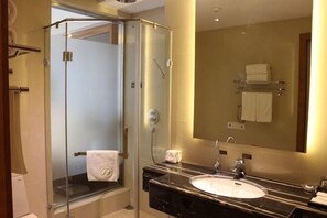 Een moderne badkamer met een douchecabine van glas, een grote spiegel en een wastafel met een marmeren blad.