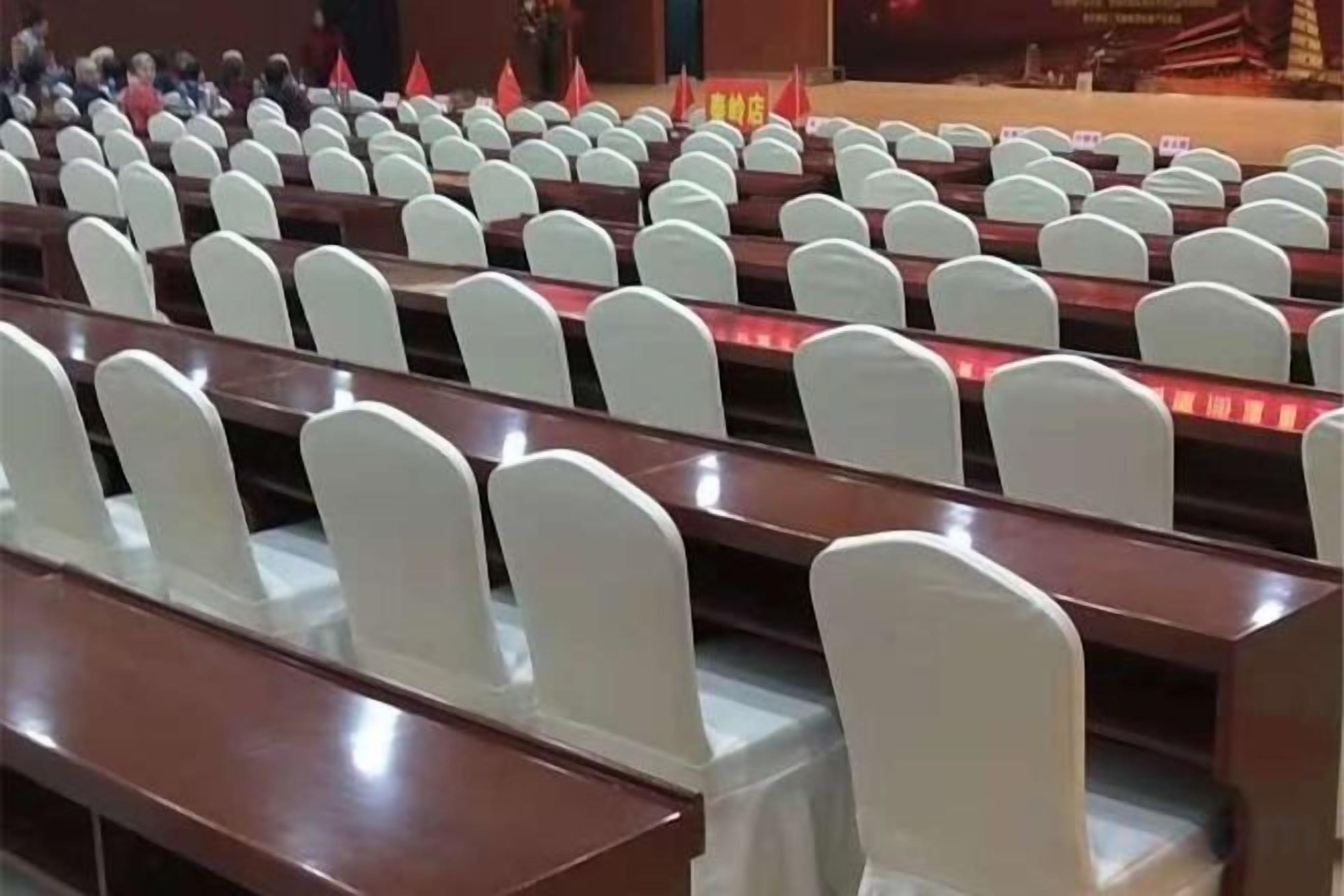 A lecture hall with rows of white chairs and wooden desks.