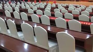 A lecture hall with rows of white chairs and wooden desks.