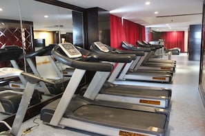 A row of treadmills in a gym with a mirrored wall and red curtains in the background. - Haocheng International Hotel (Sanyuan)