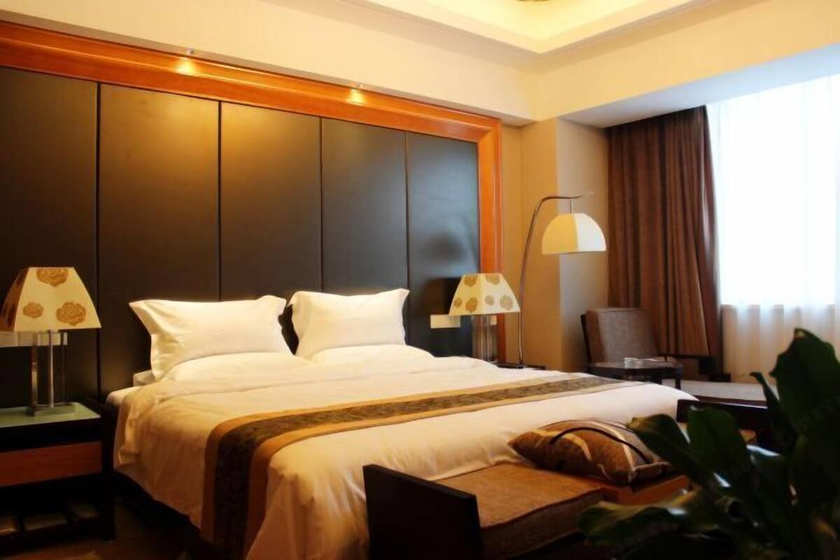 Een hotelkamer met een groot bed, twee nachtkastjes met lampen, een stoel en een raam met gordijnen.