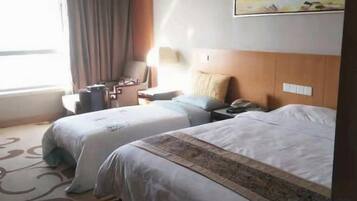 A hotel room with two beds, a desk, a chair, a lamp, and a window with curtains.