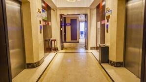 A hotel lobby with a marble floor, two elevators, a trash bin, and a light fixture. - Haocheng International Hotel (Sanyuan)