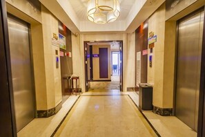 Een hotel lobby met een marmeren vloer, twee liften, een prullenbak en een lamp.