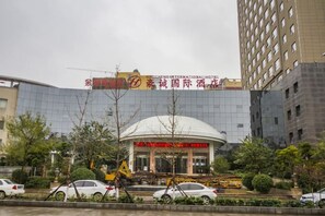 A hotel with a modern glass facade, a prominent entrance with a red sign, and a dome-shaped structure in the background. - Haocheng International Hotel (Sanyuan)