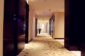 Pasillo de hotel con piso alfombrado, puertas a ambos lados y una planta al fondo.