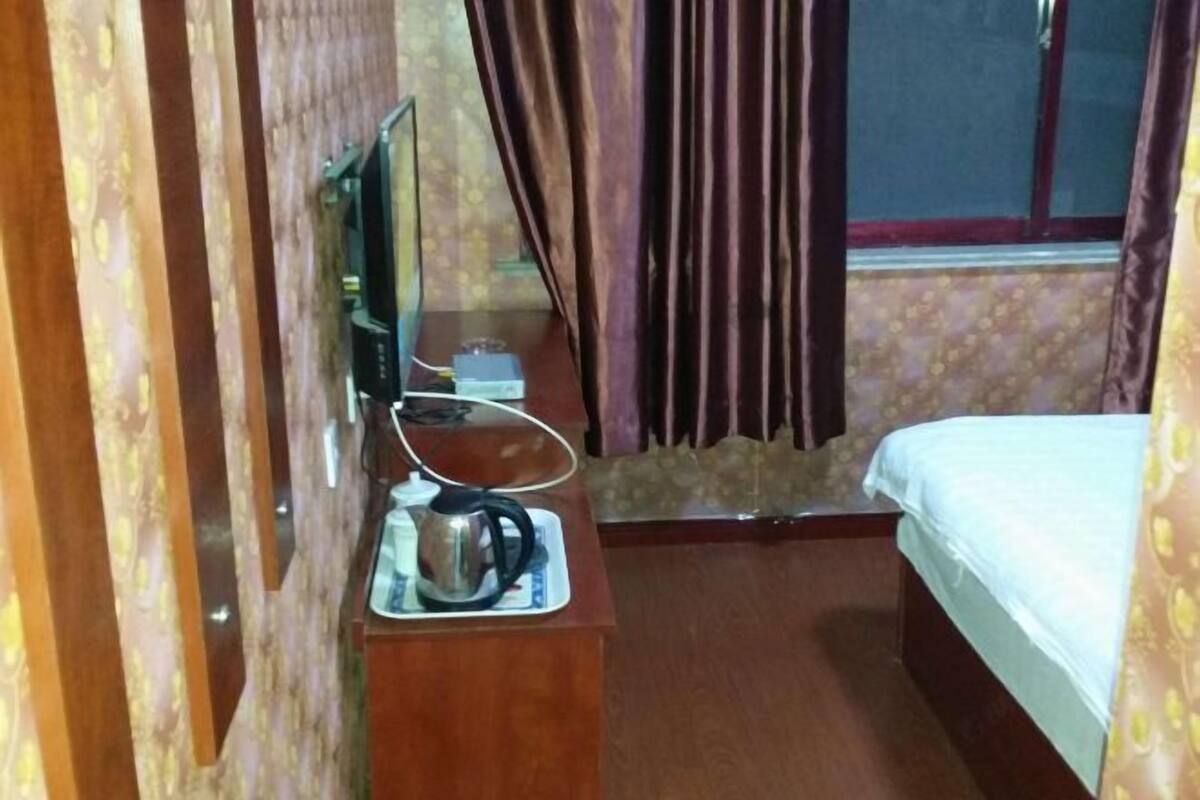 Une chambre d’hôtel avec un lit, une petite table avec une bouilloire, une télévision et des rideaux.