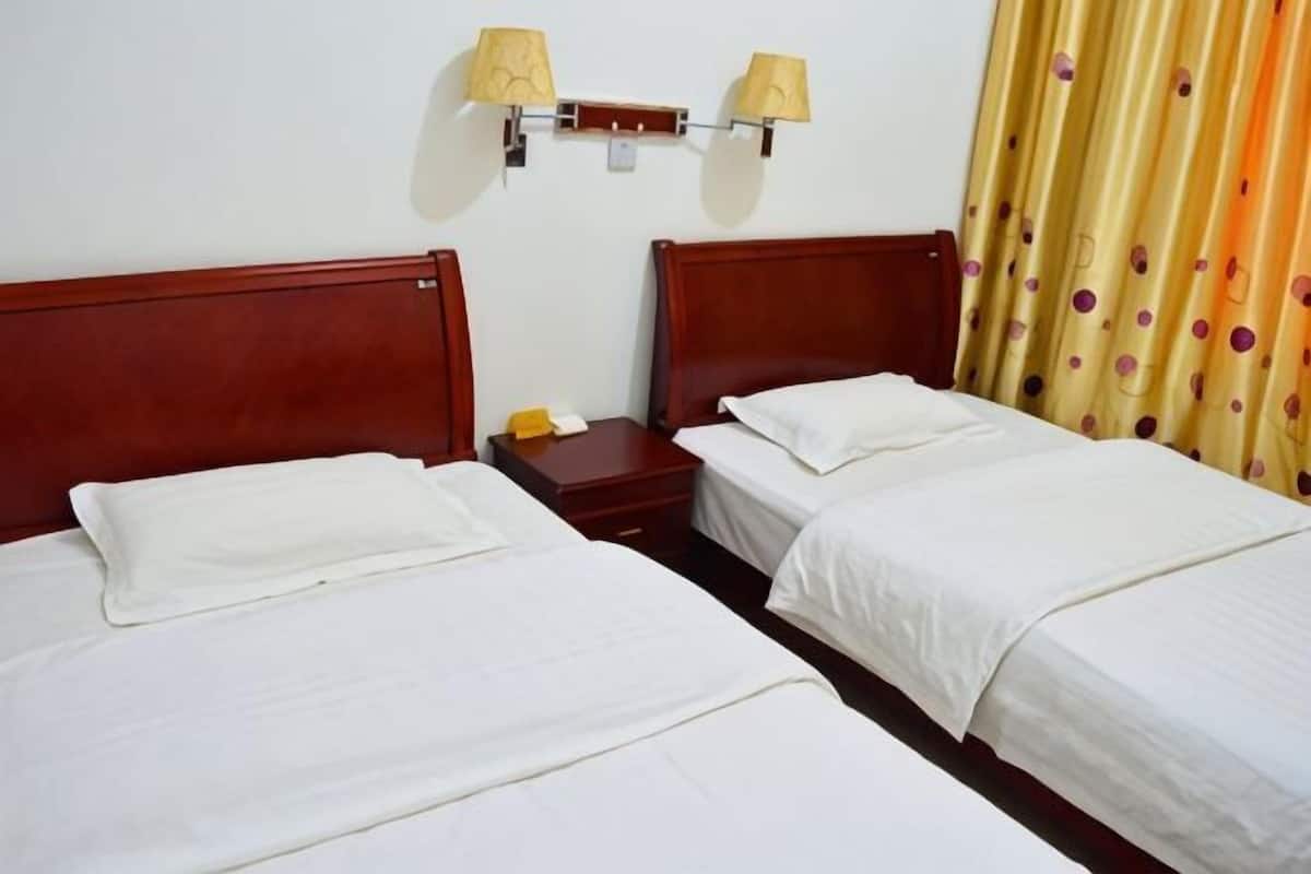 Une chambre d’hôtel avec deux lits simples, une table de chevet avec une lampe et un rideau à motifs à pois.