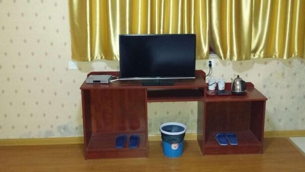 Un escritorio de madera con una computadora portátil, un estante pequeño con un hervidor, tetera y tazas, y un cubo azul con pantuflas.