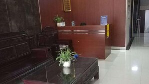 A reception area with a wooden reception desk, a glass-top coffee table with a potted plant, and a dark wooden sofa. - Haiyan Guyun Inn (Haiyan)
