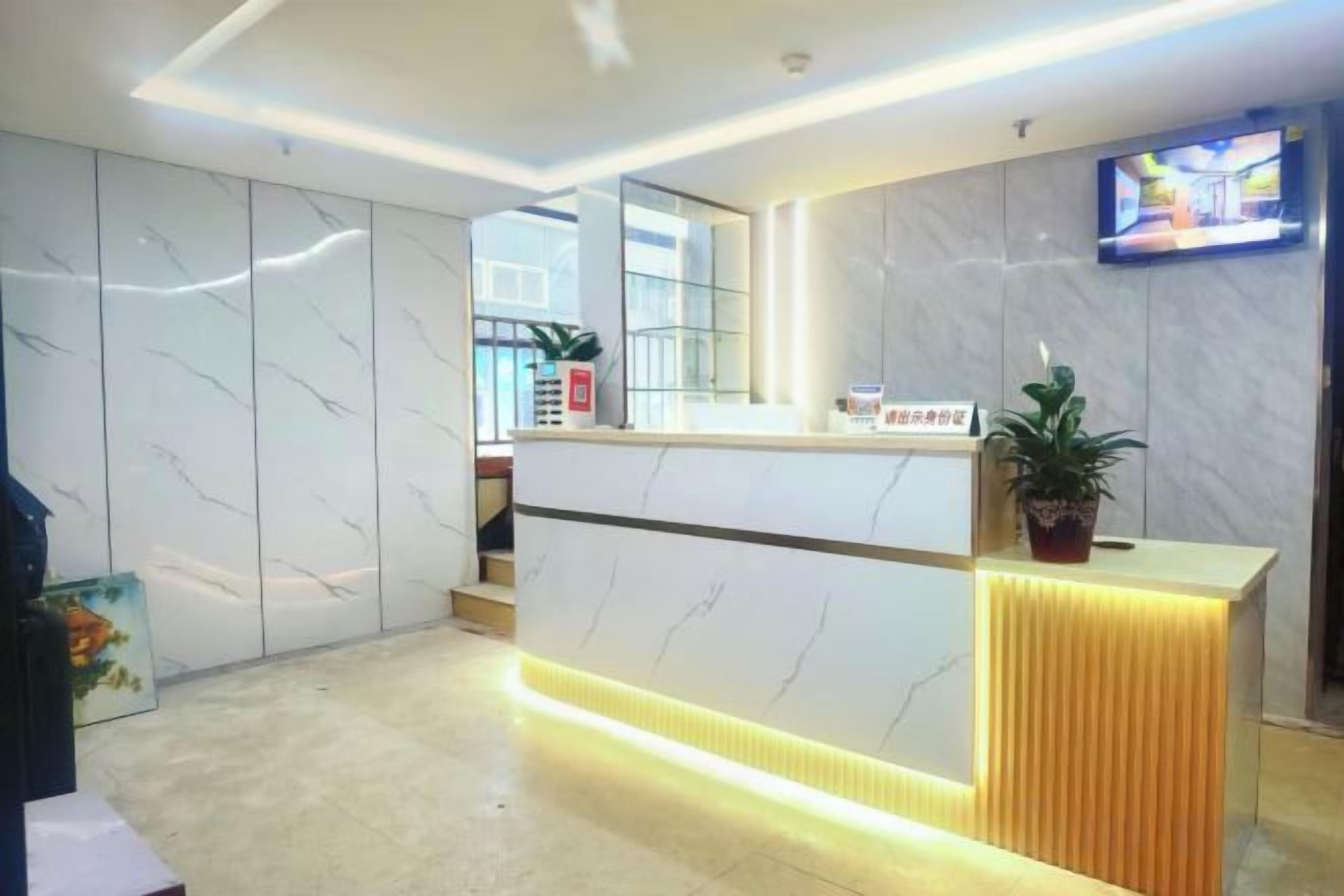 A reception area with a marble wall, a reception desk, a television, and a potted plant.
