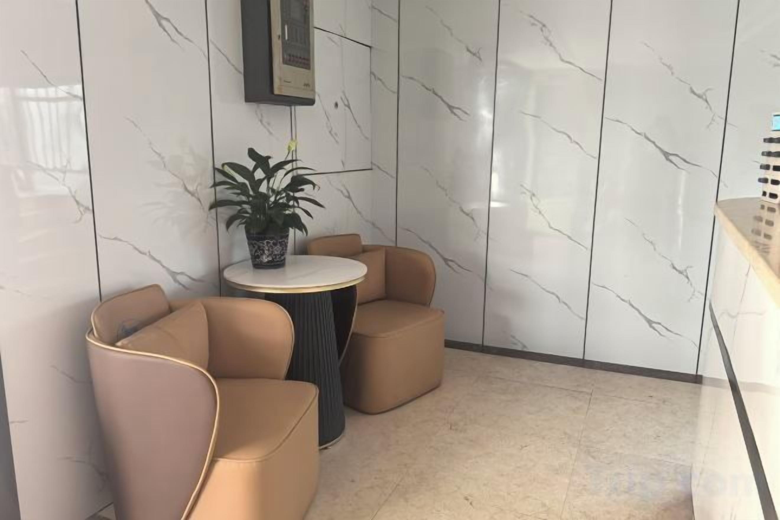 A corner with two beige armchairs, a small round table, and a potted plant.