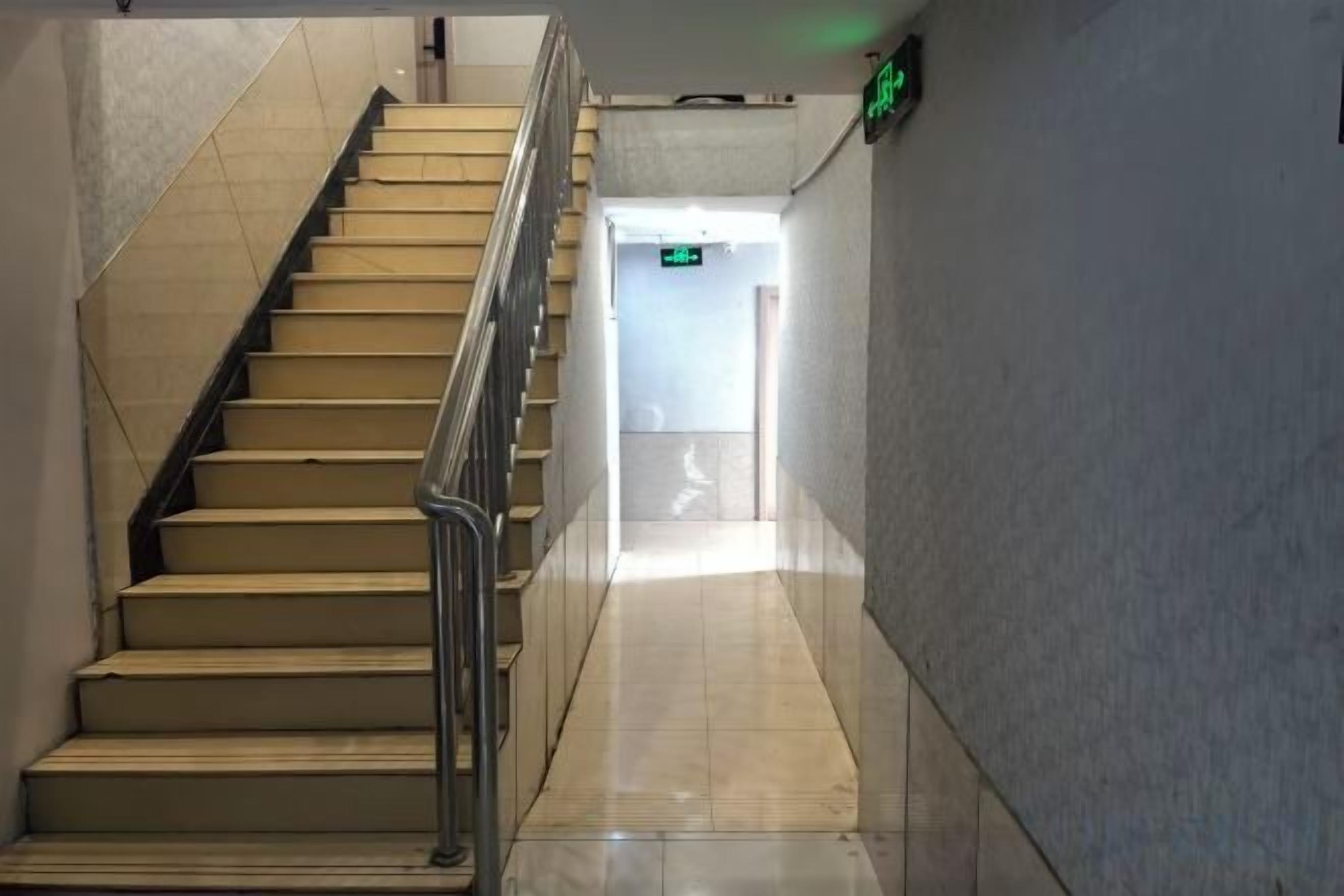 A staircase with a handrail leading to a landing, a wall with a light switch, and a door at the end of the hallway.