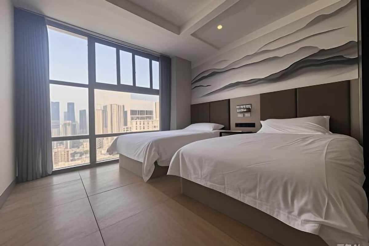 A hotel room with two beds, a large window with a city view, and a textured wall design.
