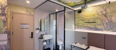 Ein modernes Hotelzimmer mit einer gläsernen Dusche, einem großen Bett, einem Nachttisch und einem an der Wand montierten Projektor.