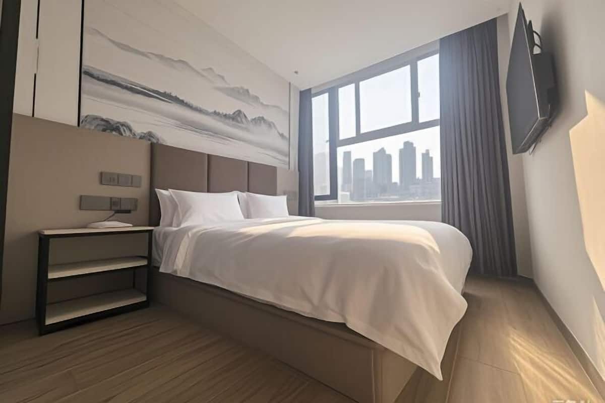 A modern hotel room with a large bed, a city view, a mounted TV, and a minimalist design.