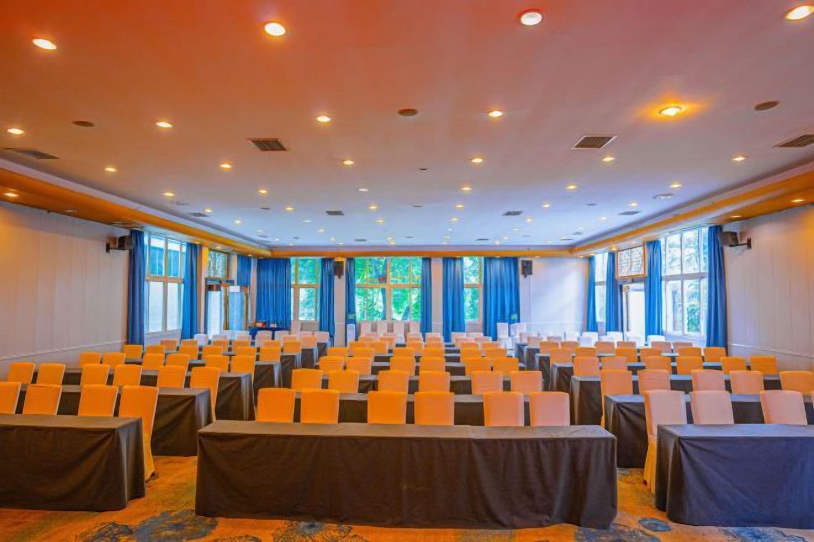 Een congreszaal met rijen stoelen, een podium en grote ramen.