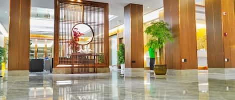 A modern lobby with a polished marble floor, a reception desk, and a decorative wall with a circular mirror.