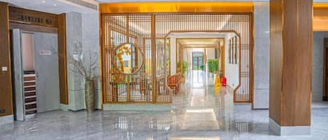 A hotel lobby with a modern design, featuring a central reception desk, a glass elevator, and a decorative wooden partition.
