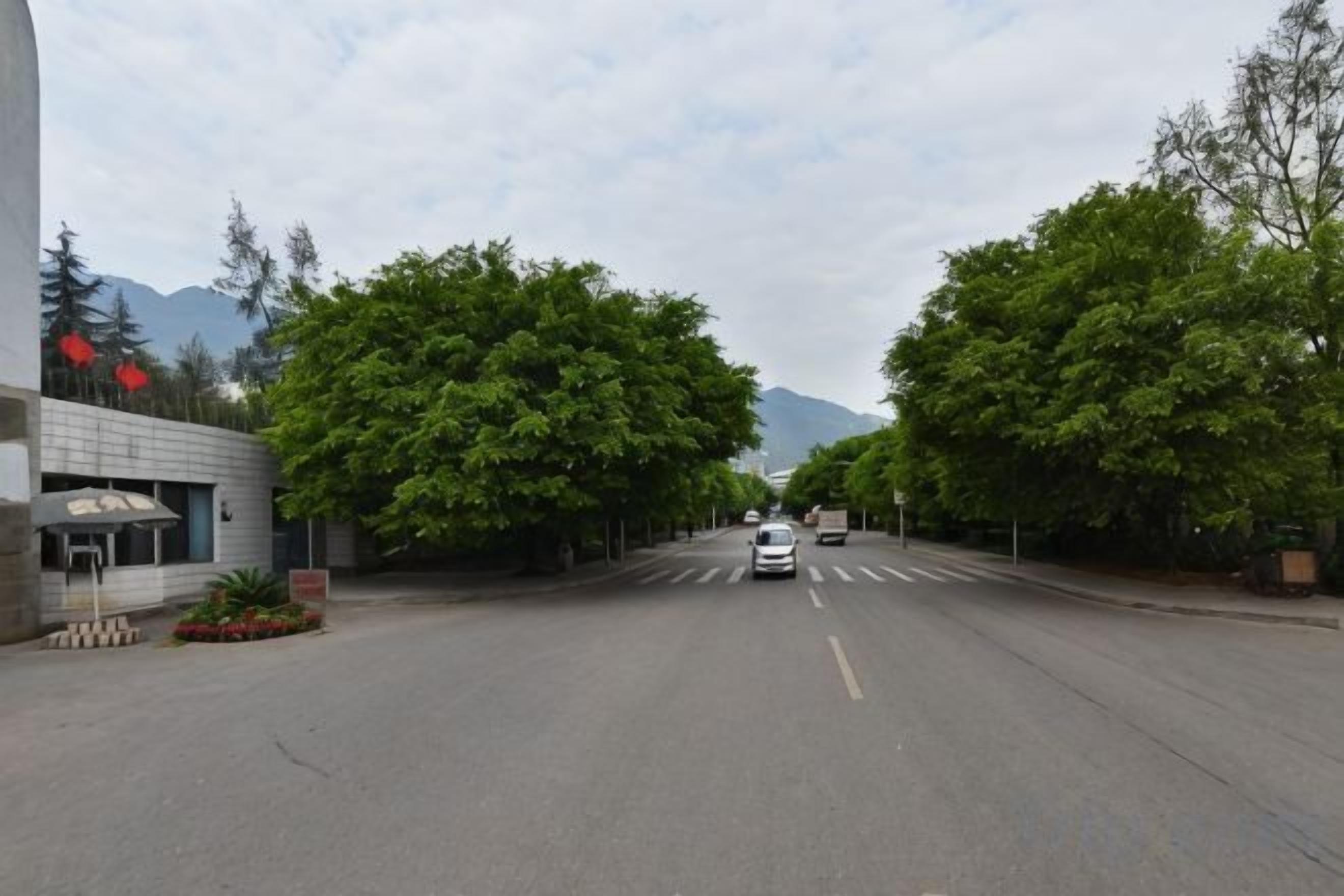 Una calle con un edificio a la izquierda, árboles a lo largo de la carretera y un coche a lo lejos.