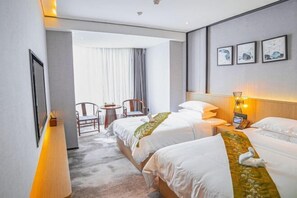 Ein Hotelzimmer mit zwei Betten, einem Schreibtisch, einem Stuhl, einem kleinen Tisch und einem Fenster mit Vorhängen.