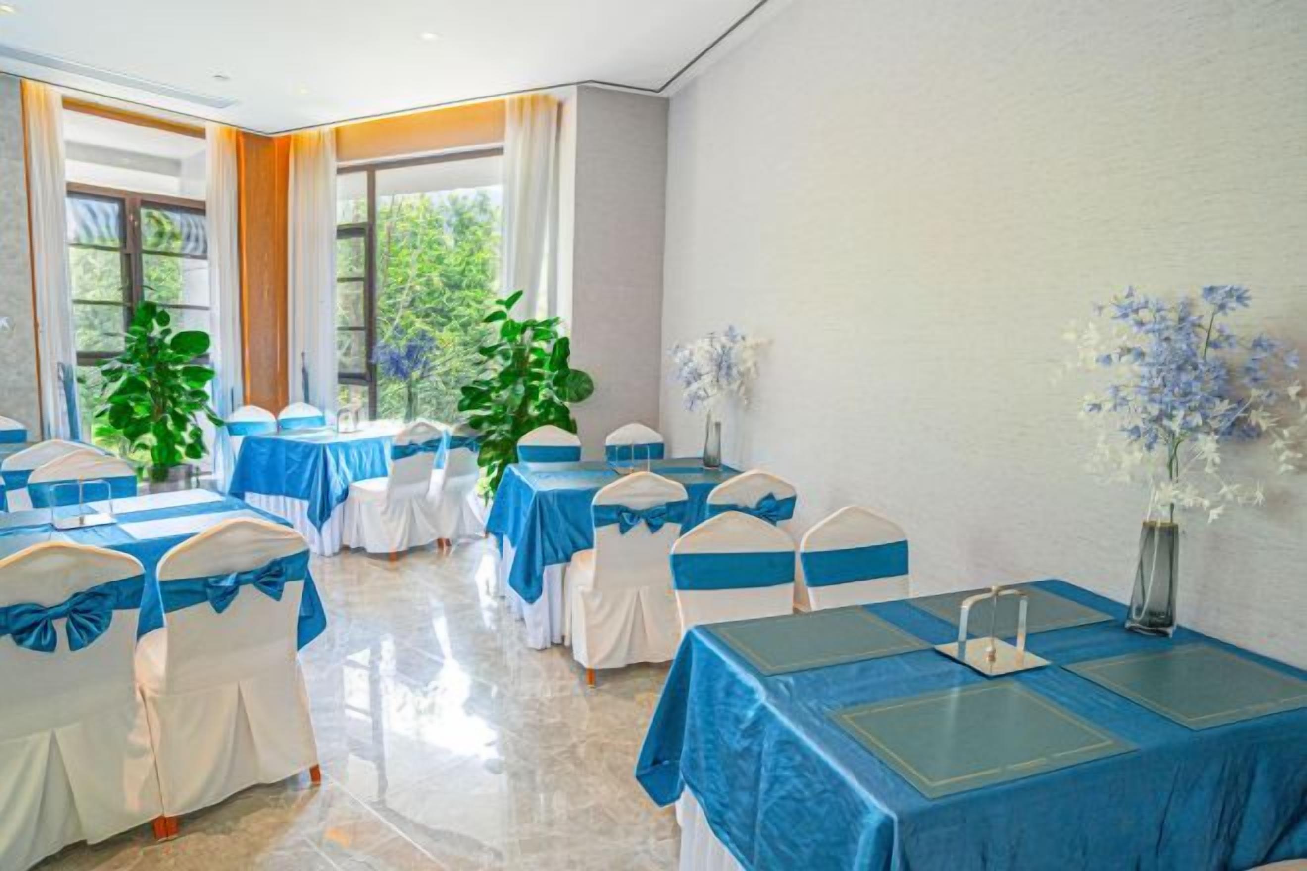 A conference room with tables and chairs, large windows, and indoor plants.