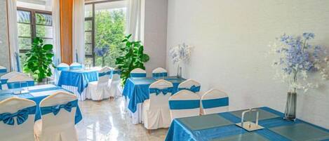 A conference room with tables and chairs, large windows, and indoor plants.