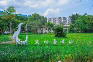 A green field with a white bird sculpture and Chinese characters, a pathway, and a building in the background. - egret land Hotel (Chongqing)