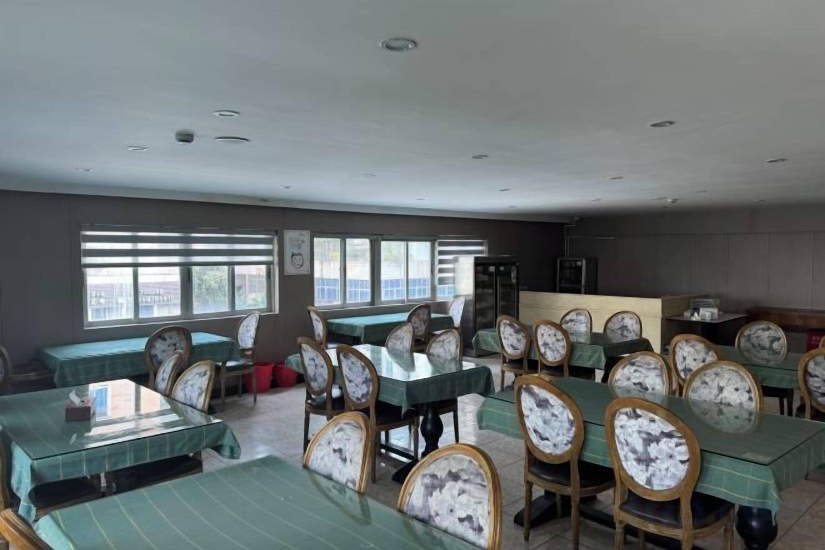 A dining area with tables and chairs, large windows, and a view of the outside.