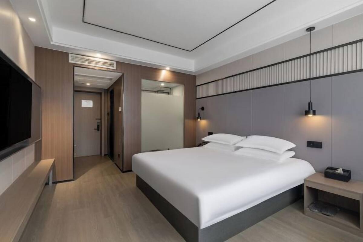 Une chambre d’hôtel moderne dotée d’un grand lit, de tables de chevet, d’un téléviseur à écran plat et d’un dressing.