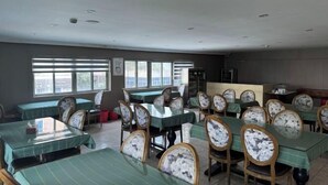 Zona pranzo con diversi tavoli e sedie, ampie finestre e una cucina sullo sfondo.