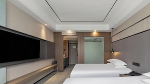 Camera d'albergo moderna con TV a schermo piatto, due letti, un armadio a muro e un bagno visibile tramite una porta in vetro.