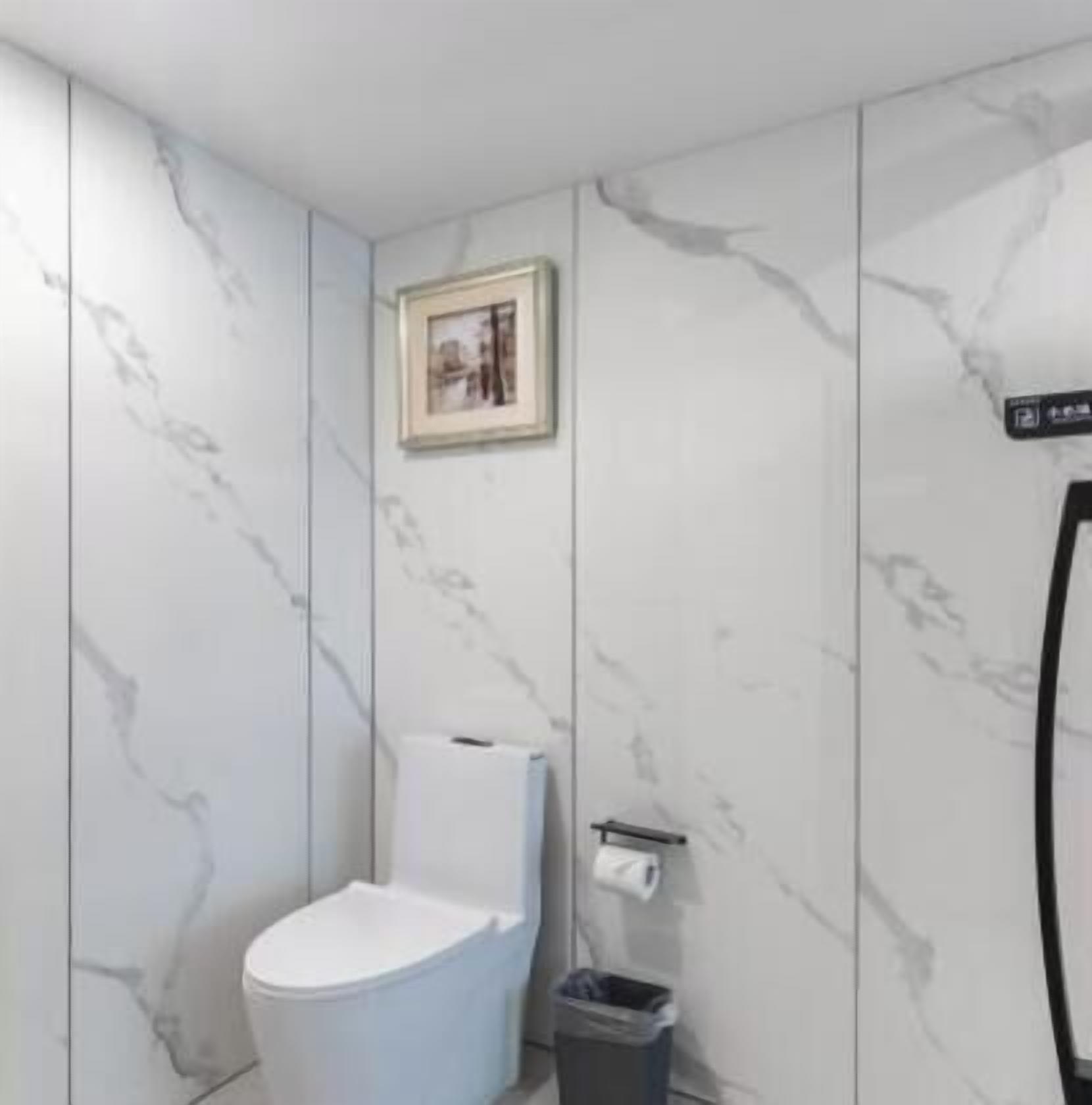 Un baño con paredes de mármol, un inodoro, un cubo de basura y un cuadro en la pared.