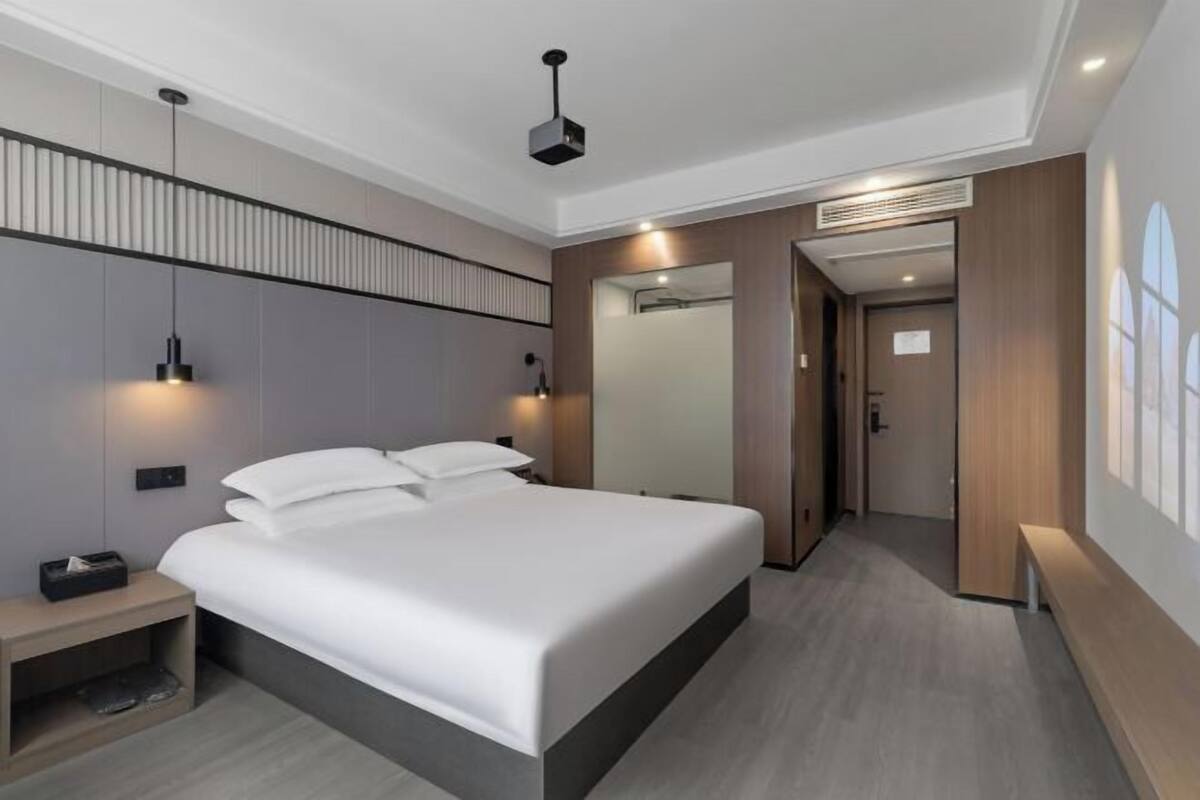 Une chambre d’hôtel moderne avec un grand lit, des lampes de chevet, une table de chevet, un miroir et une porte donnant sur une autre pièce.
