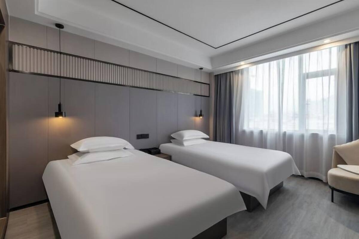Une chambre d’hôtel avec deux lits simples, un canapé et une grande fenêtre avec des rideaux.