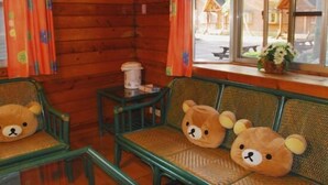 Een houten interieur met houten wanden, een raam met uitzicht op een houten huis, en drie stoelen met berenvormige kussens.