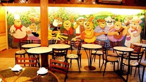 Een restaurant met houten tafels en stoelen, een muurschildering met tekenfilmfiguren en een rustiek plafond.