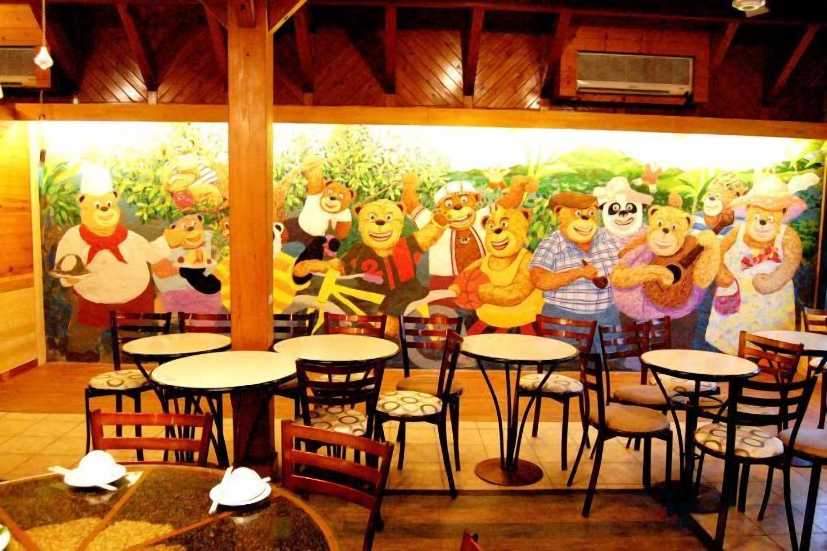 Un restaurante con terraza y un mural de personajes animados. Mesas y sillas dispuestas para comer.