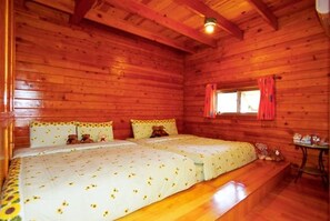 Une chambre de style cabane avec deux lits, des murs en bois, une fenêtre avec des rideaux rouges et une petite table sur laquelle sont posés quelques objets.